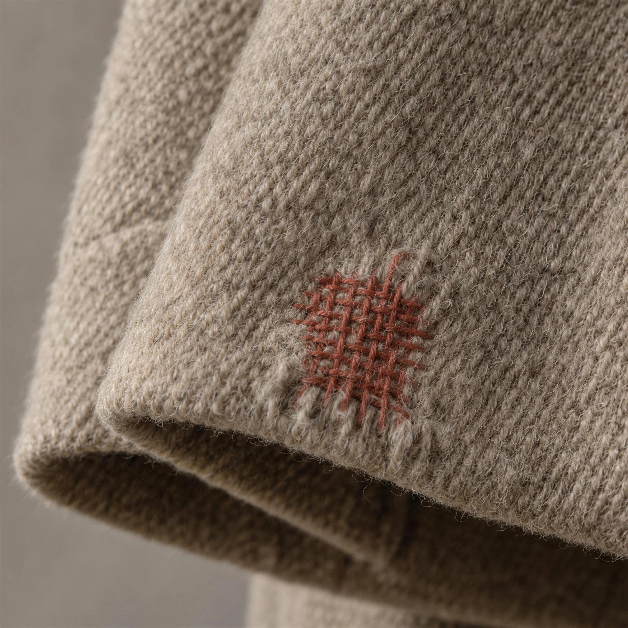 A recycled-wool cuff darned in rust-red thread, the mend left visible on purpose